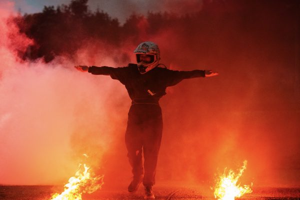 Kneebone Cadillac. Actor in racing helmet walks out of a fire.