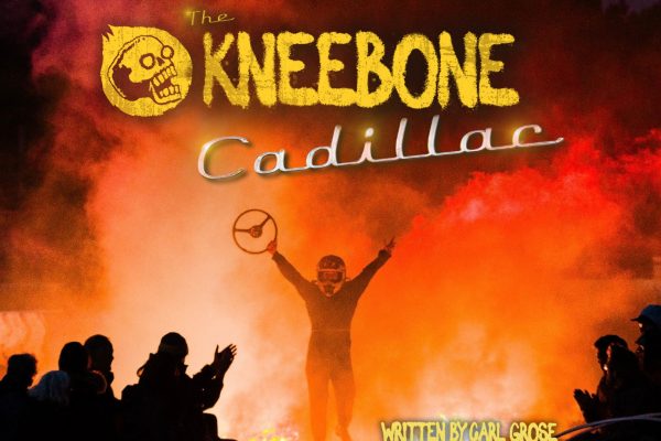 The Kneebone Cadillac. Maddie emerges from the flames and smoke holding a steering wheel high. She is wearing a helmet. In the foreground you can see the audience silhouetted.