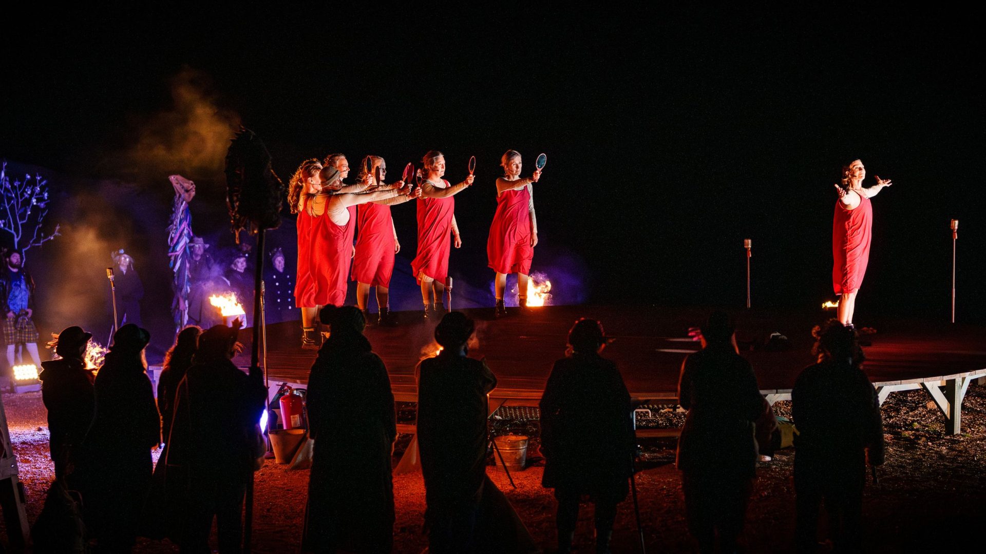 Performers in red dresses hold up hand held mirrors - Wildworks Stranger Beast