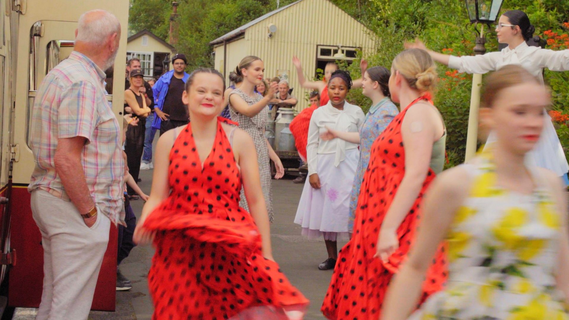 Pupils from Bodmin College dancing and performing in bright red dresses in Departures and Arrivals at Bodmin and Wenford Railway as part of Wildworks Theatre's Hello Stranger Project.