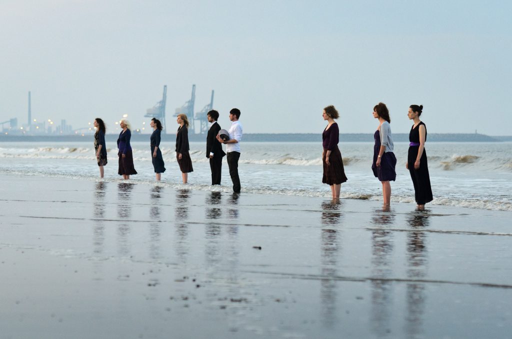 Dawn. Waiting for the Baptism. Performers are ankle deep in the water. The Passion of Port Talbot by Wildworks