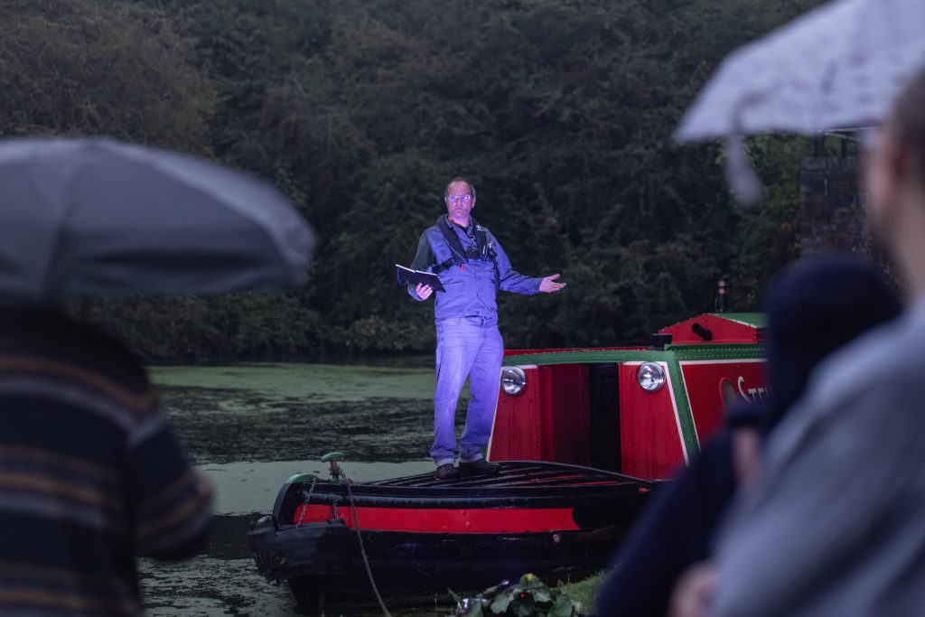 A man stands on a canal boat performing.