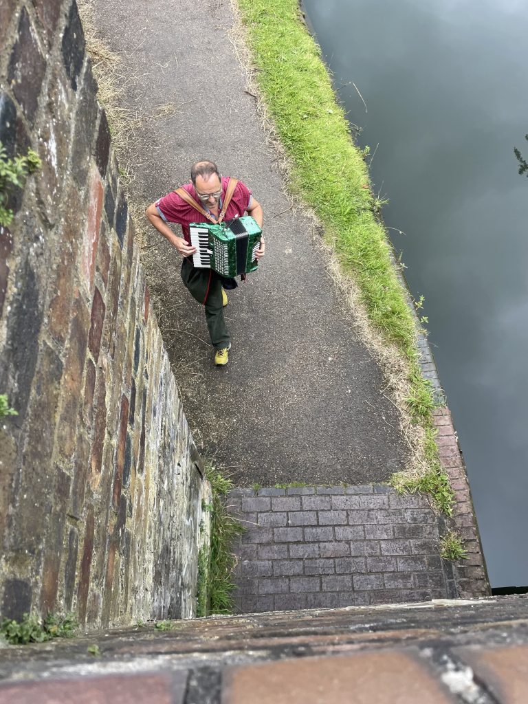 A man is walking along the canal playing an accordian.