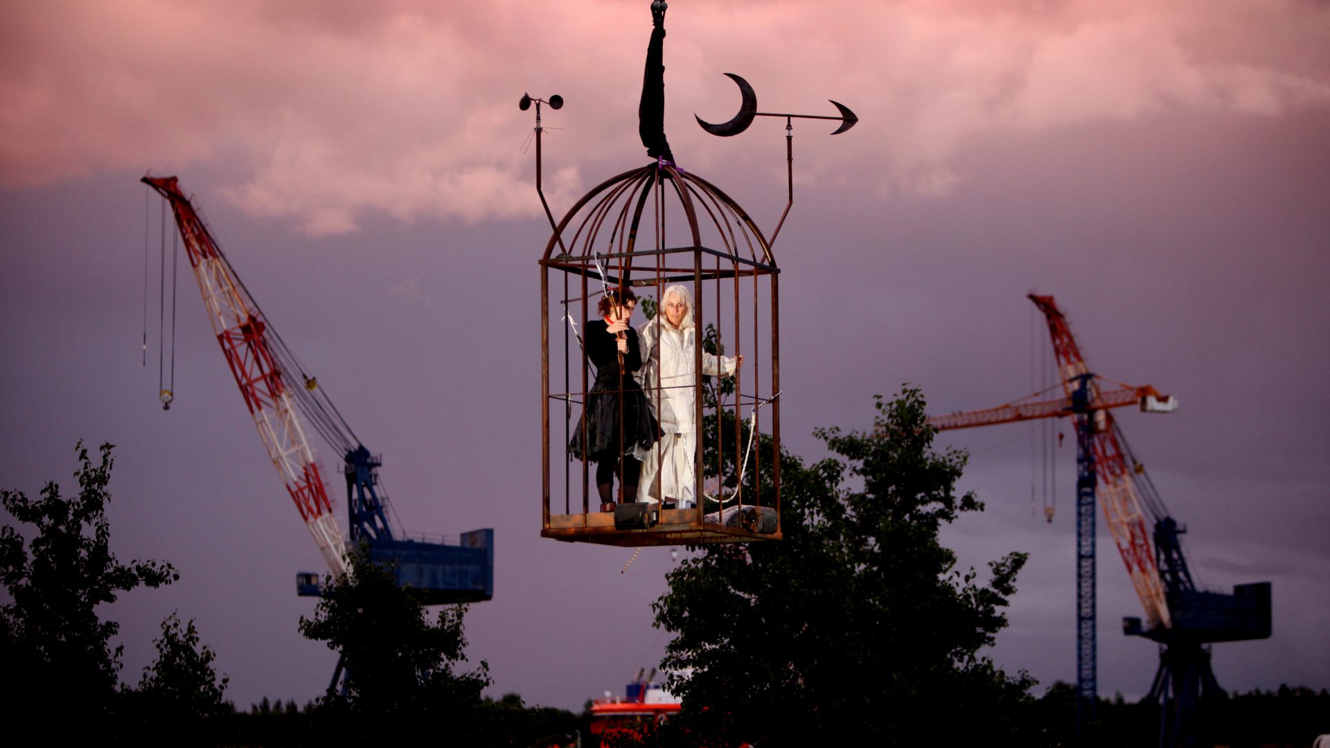 Two performers are in a huge cage suspended in the air. A Beautiful Journey by Wildworks