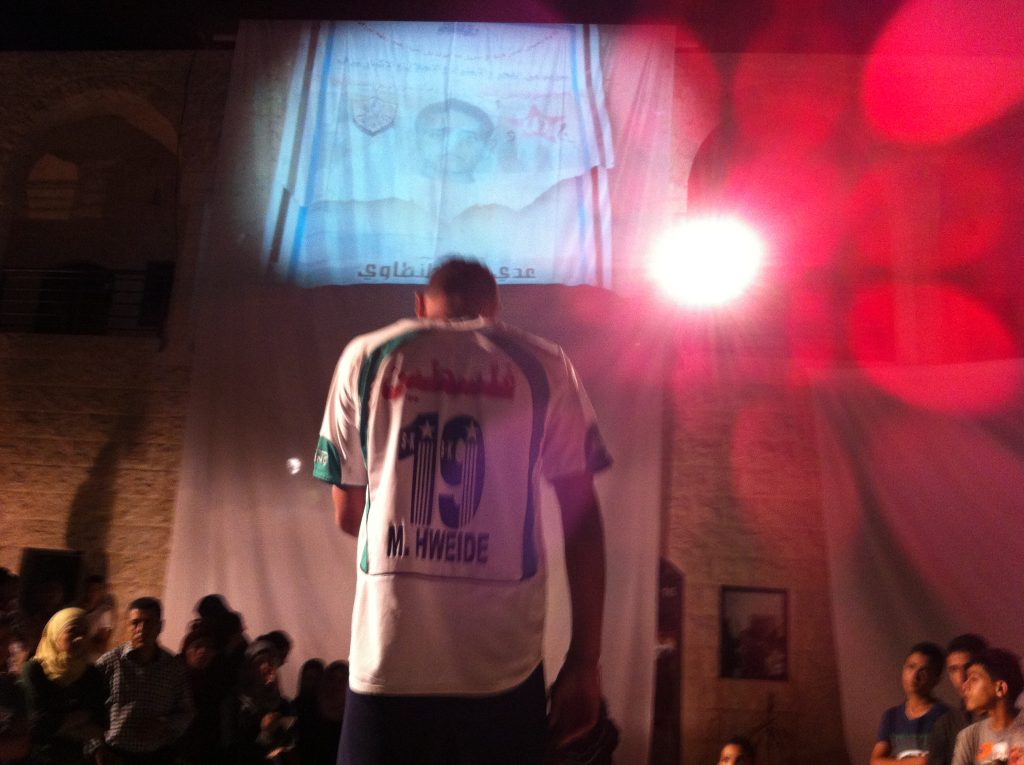 A young man called Mohammed performs in front of a projected image of his friend, Odai, who was killed. Nablus, City of Stories by Wildworks
