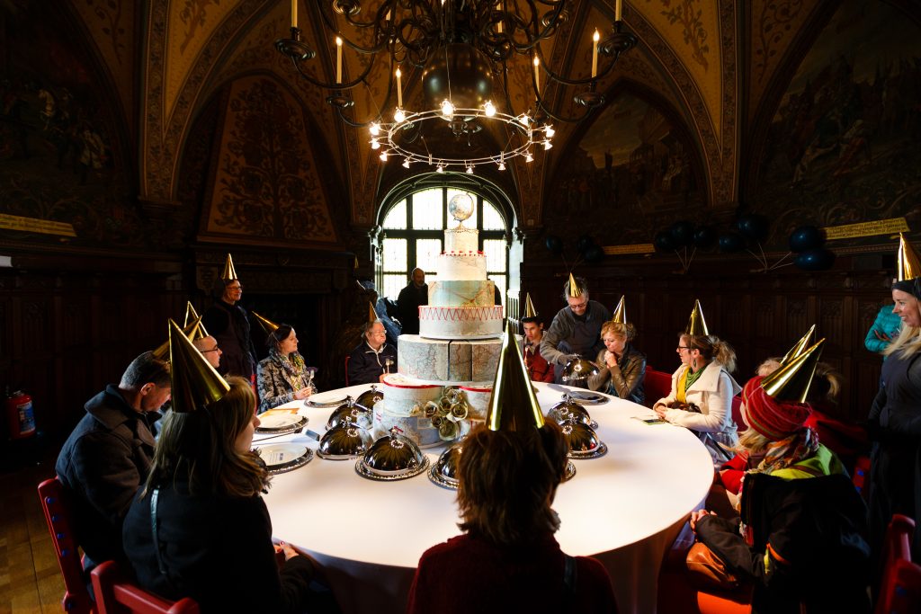 A huge cake sits in the centre of a round table. Once and Twice Upon a Castle by Wildworks.