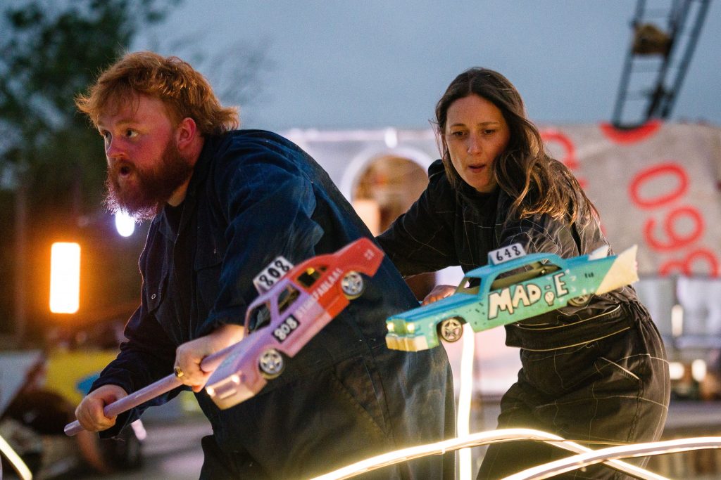 Two actors hold model cars during the race scene of 'The Kneebone Cadillac'