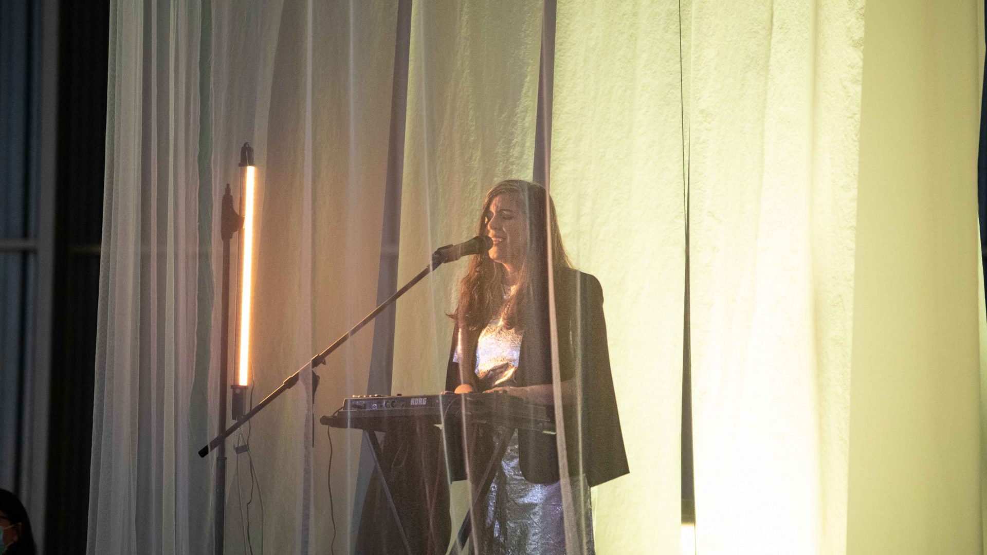 Keyboard player lit up with light yellow light. Arrow of time set in Malta Aviation Museum in Ta' Qali with Wildworks and Etnika, Magna Żmien, Buena Sombra Films
