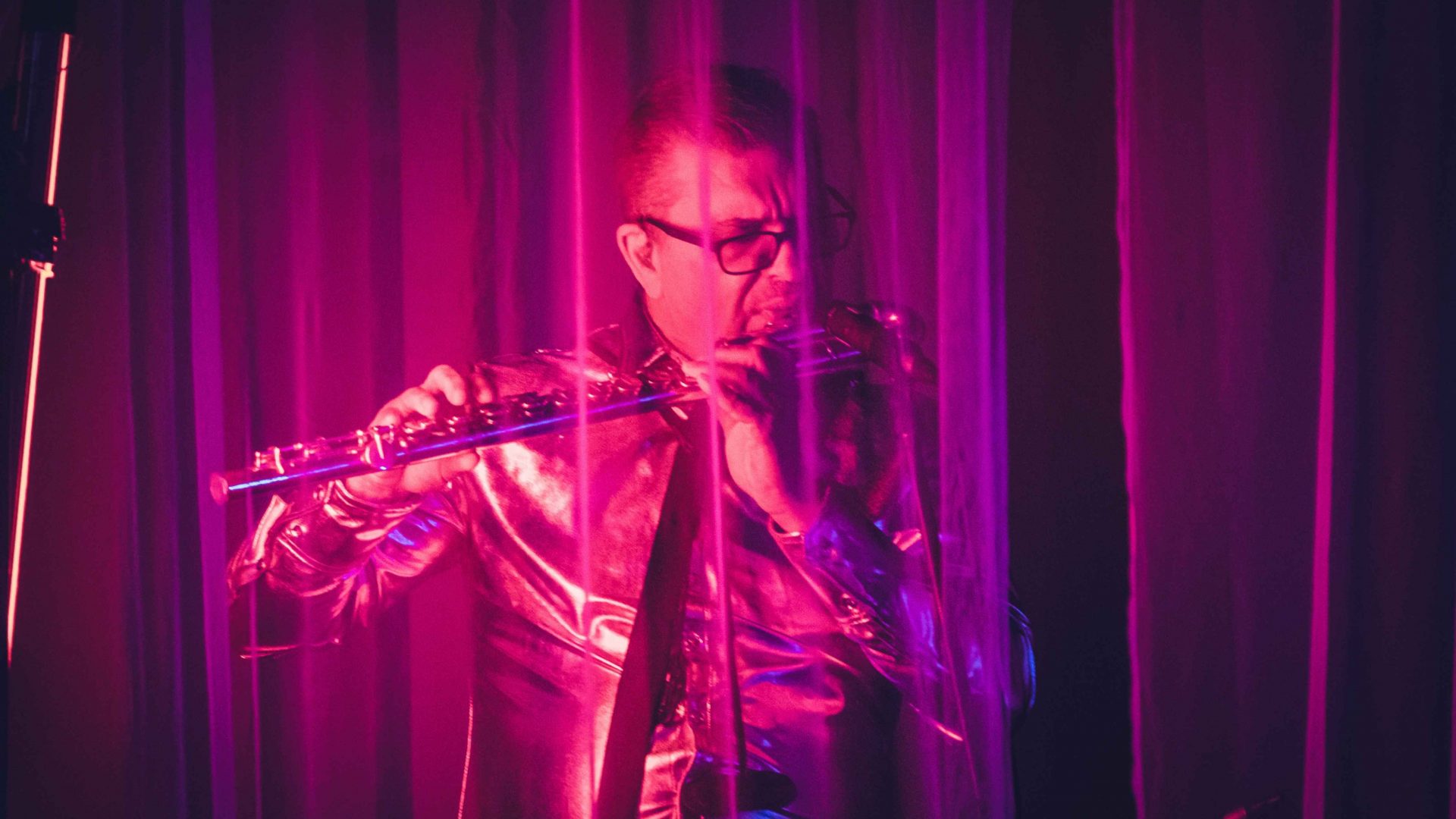 A flutist lit up with pink light. Arrow of time set in Malta Aviation Museum in Ta' Qali with Wildworks and Etnika, Magna Żmien, Buena Sombra Films