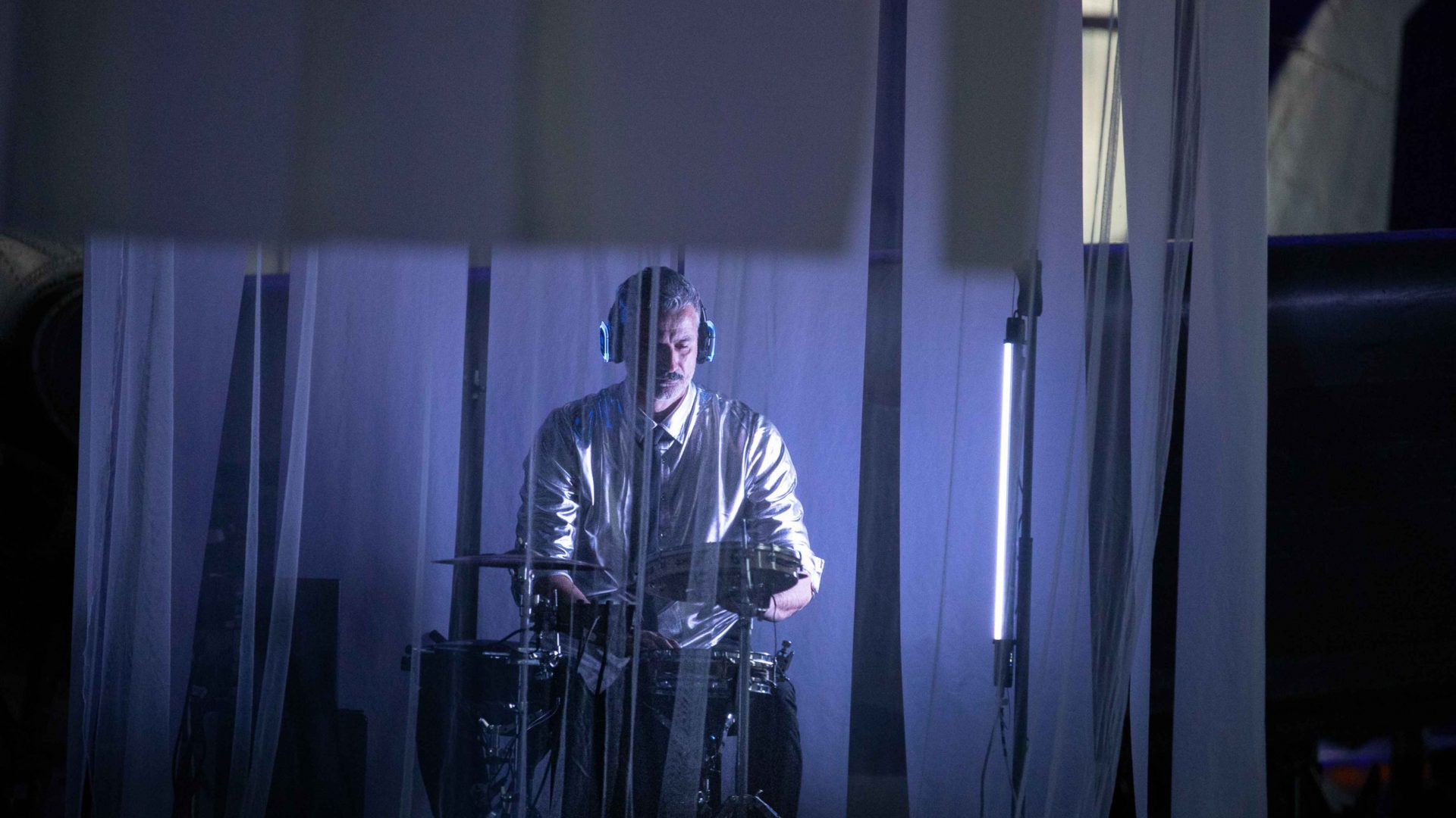 A drummer lit up on stage. Arrow of time set in Malta Aviation Museum in Ta' Qali with Wildworks and Etnika, Magna Żmien, Buena Sombra Films