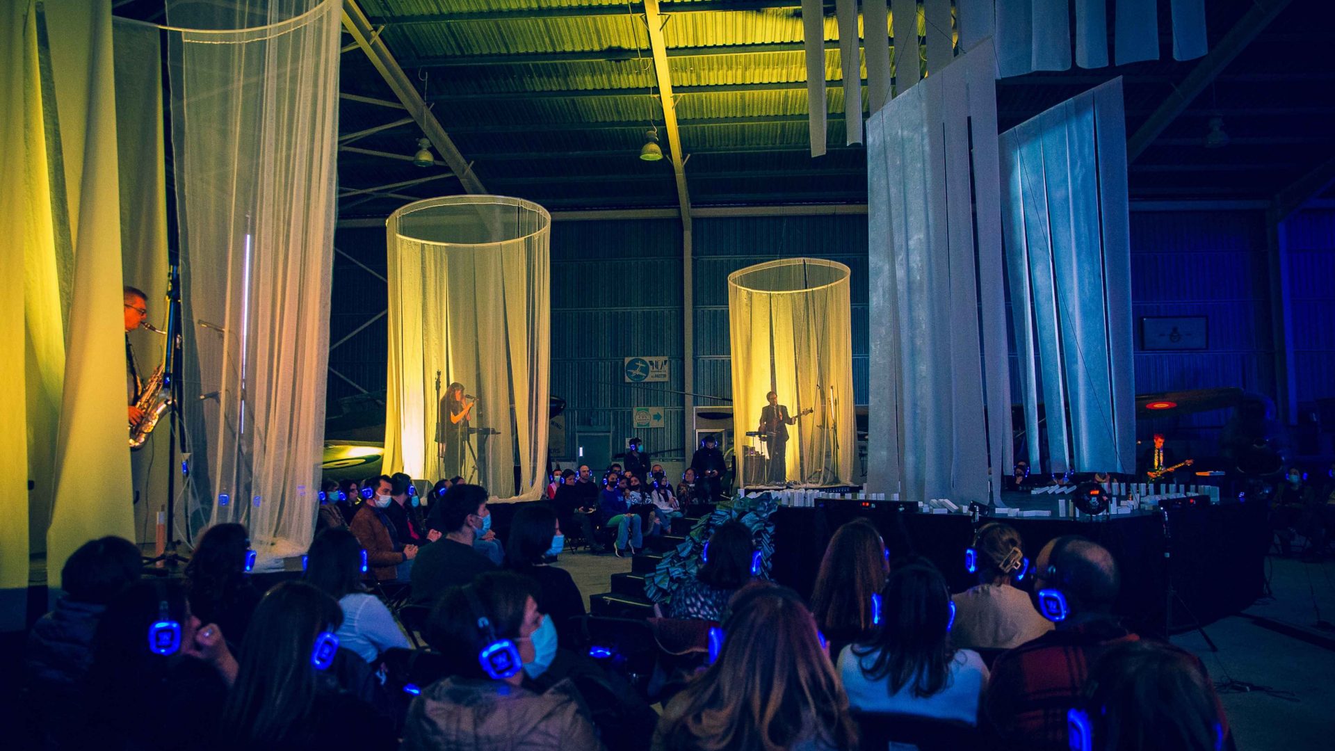 two musicians on the stage lit up with yellow light. Arrow of time set in Malta Aviation Museum in Ta' Qali with Wildworks and Etnika, Magna Żmien, Buena Sombra Films