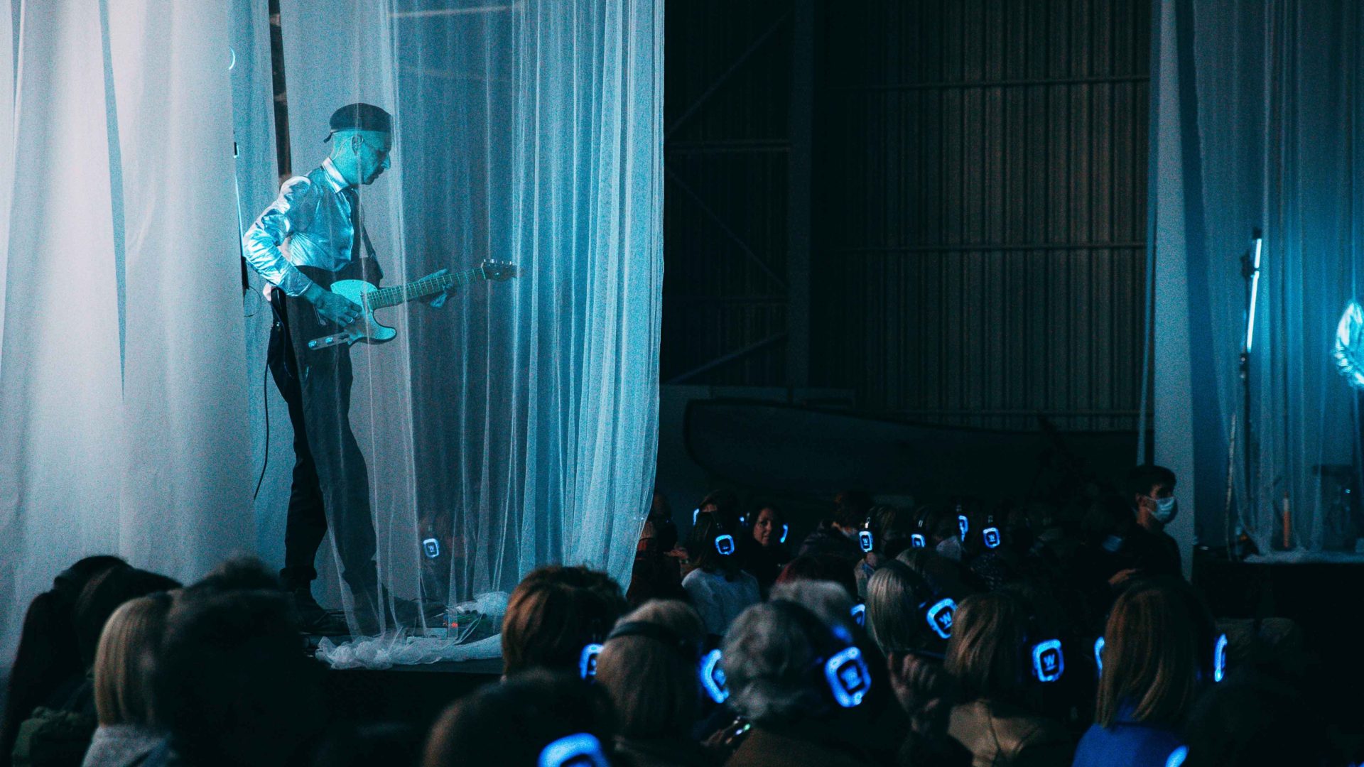 Guitar player lit up with blue light on the stage. Arrow of time set in Malta Aviation Museum in Ta' Qali with Wildworks and Etnika, Magna Żmien, Buena Sombra Films