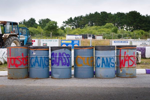 Old oil barrels in a line. They are each spray painted with labels for waste disposal.