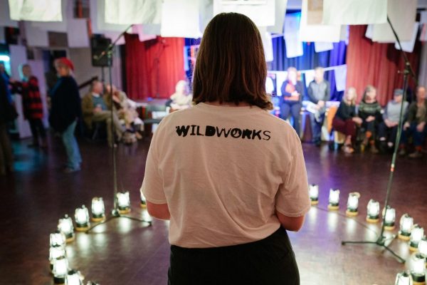 Izzy stood with her back to the camera. She is wearing a Wildworks t-shirt and stood in front of a circle of lanterns.