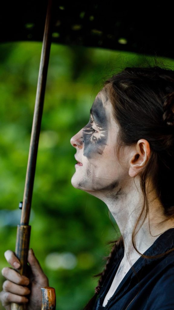 Izzy in Wolf's Child standing under an umbrella. 