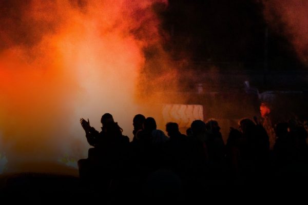 A photo of an audience in front of fire and smoke. They are silhouetted .