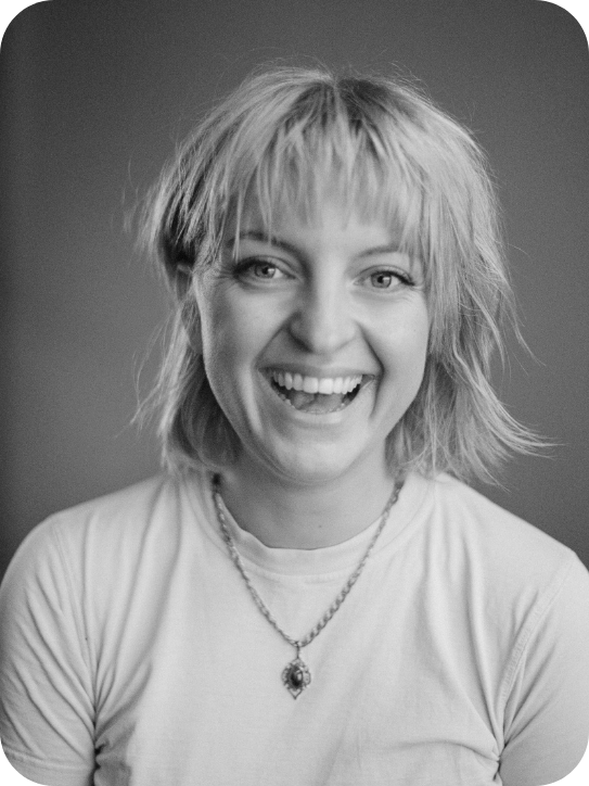 Black and White images of Millie Faraway. She is wearing a white t-shirt, her hair is a short bob and she is smiling at the camera.